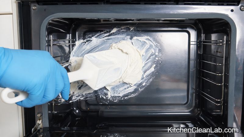 Applying baking soda paste to a dirty oven wall for tough stain removal